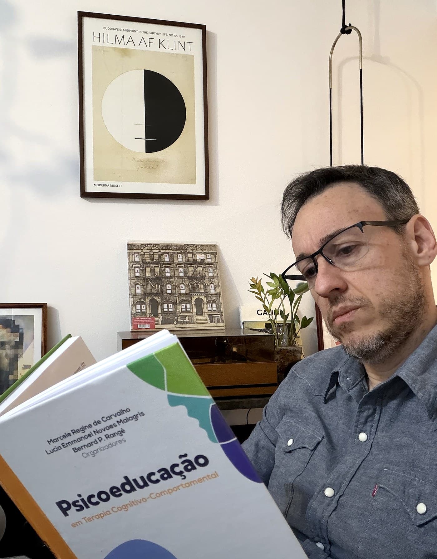 Thiago Vendramini lendo um livro de Psicoeducação em Terapia Cognitivo-Comportamental, em sua estante pessoal