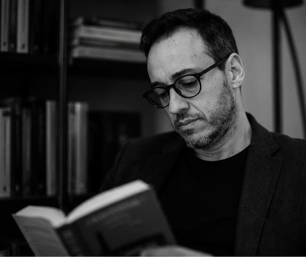 Thiago Vendramini lendo um livro em sua estante pessoal, com expressão de concentração
